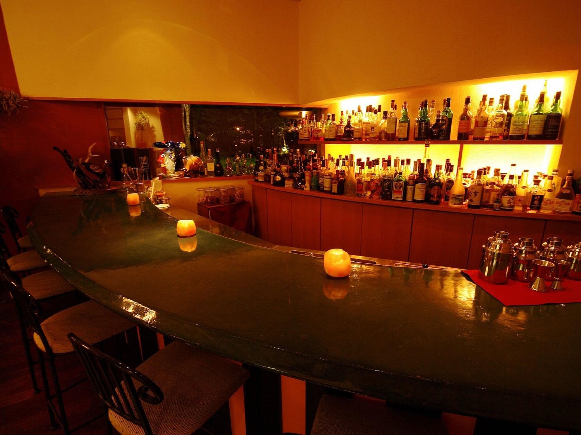 Un espace bar avec un long comptoir, de nombreuses bouteilles d’alcool et quelques bougies.
