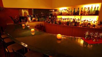Un espace bar avec un long comptoir, de nombreuses bouteilles d’alcool et quelques bougies.