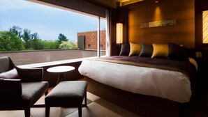 Een hotelkamer met een groot bed, een zithoek met een kleine tafel en uitzicht op het omliggende landschap.