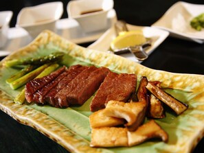 A plate of food with grilled meat, asparagus, and fried items on a green leaf. - Hokkaido Hotel (Obihiro)