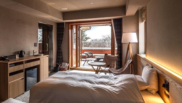 Een hotelkamer met een groot bed, een bureau met stoel, een kleine tafel met stoelen en uitzicht op de omgeving.