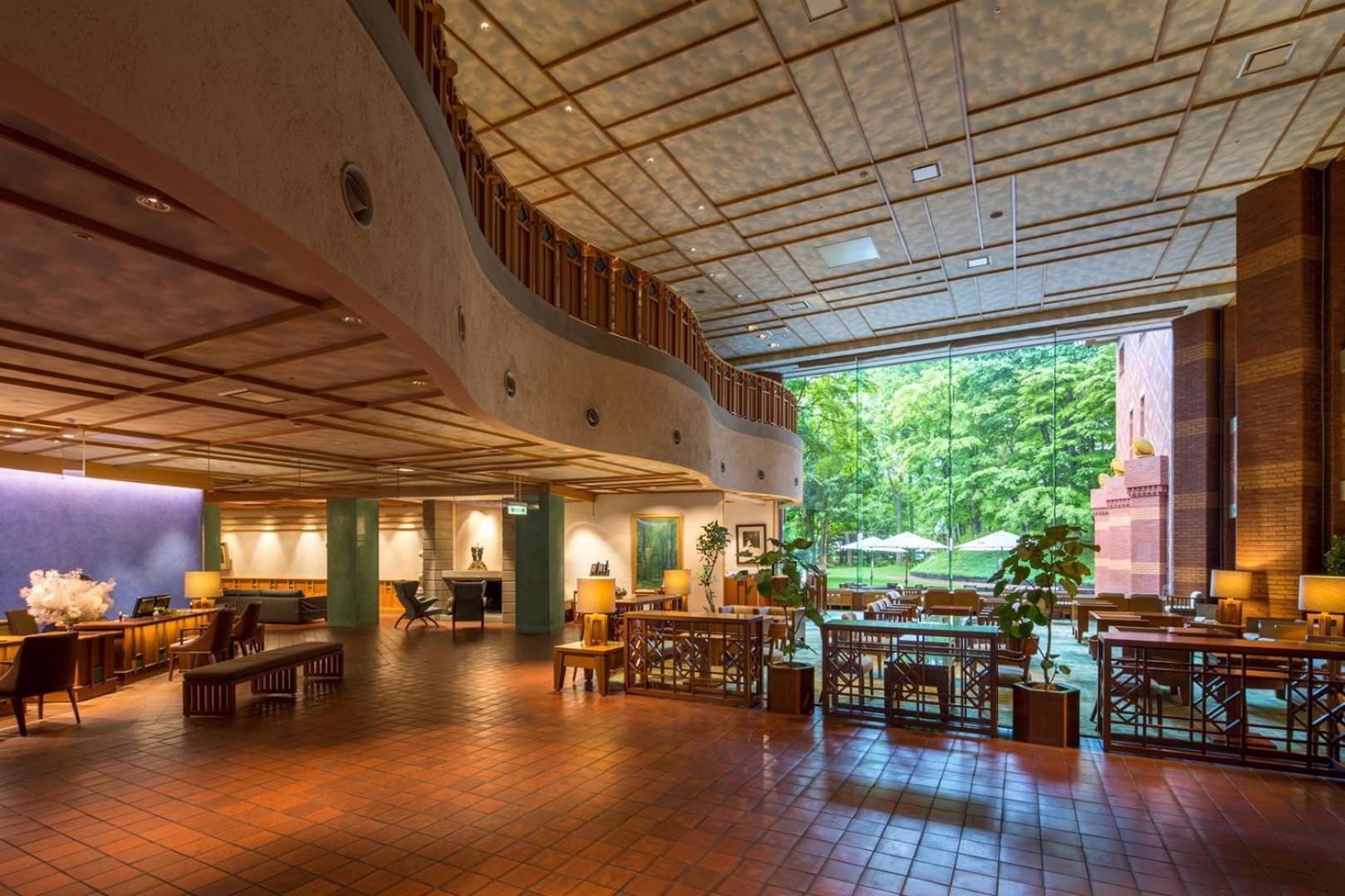 A spacious lobby with a high ceiling, a central staircase, and a view of greenery outside.