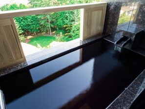 A kitchen with a black countertop and a view of a green garden through a window. - Hokkaido Hotel (Obihiro)
