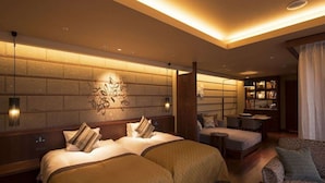 A hotel room with two beds, a sitting area with a sofa and chairs, a small table, and a bookshelf. - Hokkaido Hotel (Obihiro)