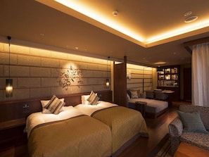 A hotel room with two beds, a sitting area with a sofa and chairs, a small table, and a bookshelf. - Hokkaido Hotel (Obihiro)