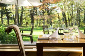 Un área de comedor al aire libre con una mesa lista para dos personas, que incluye una silla, una servilleta y copas de vino.