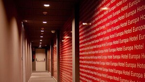A hotel corridor with a red patterned wall and a carpeted floor.