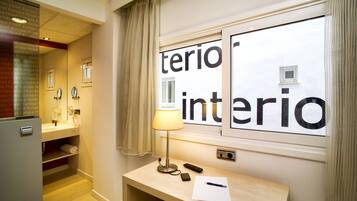 Habitación de hotel con escritorio, lámpara, espejo, toalla y ventana con la inscripción 'terio interior'.