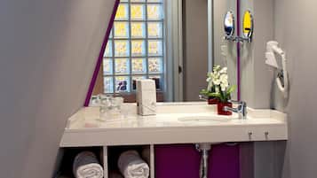 A modern bathroom with a purple accent wall, a large mirror, a hairdryer, and a shelf with towels.