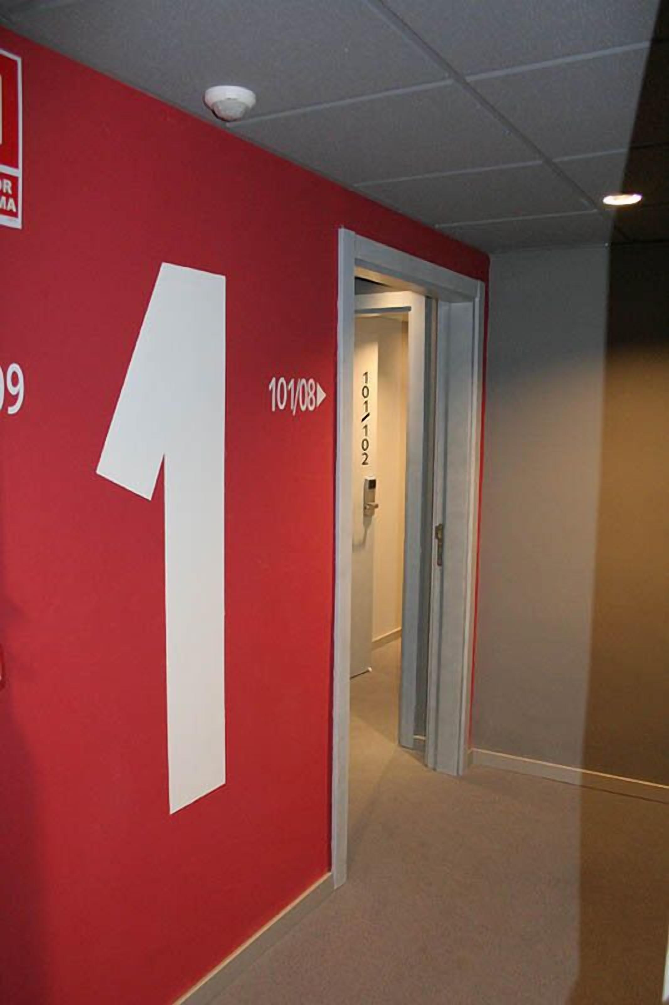 A hallway with a red wall featuring a large white number '1' and a door leading to another room.