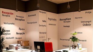 A reception desk with multilingual signage, a computer, and a plant.