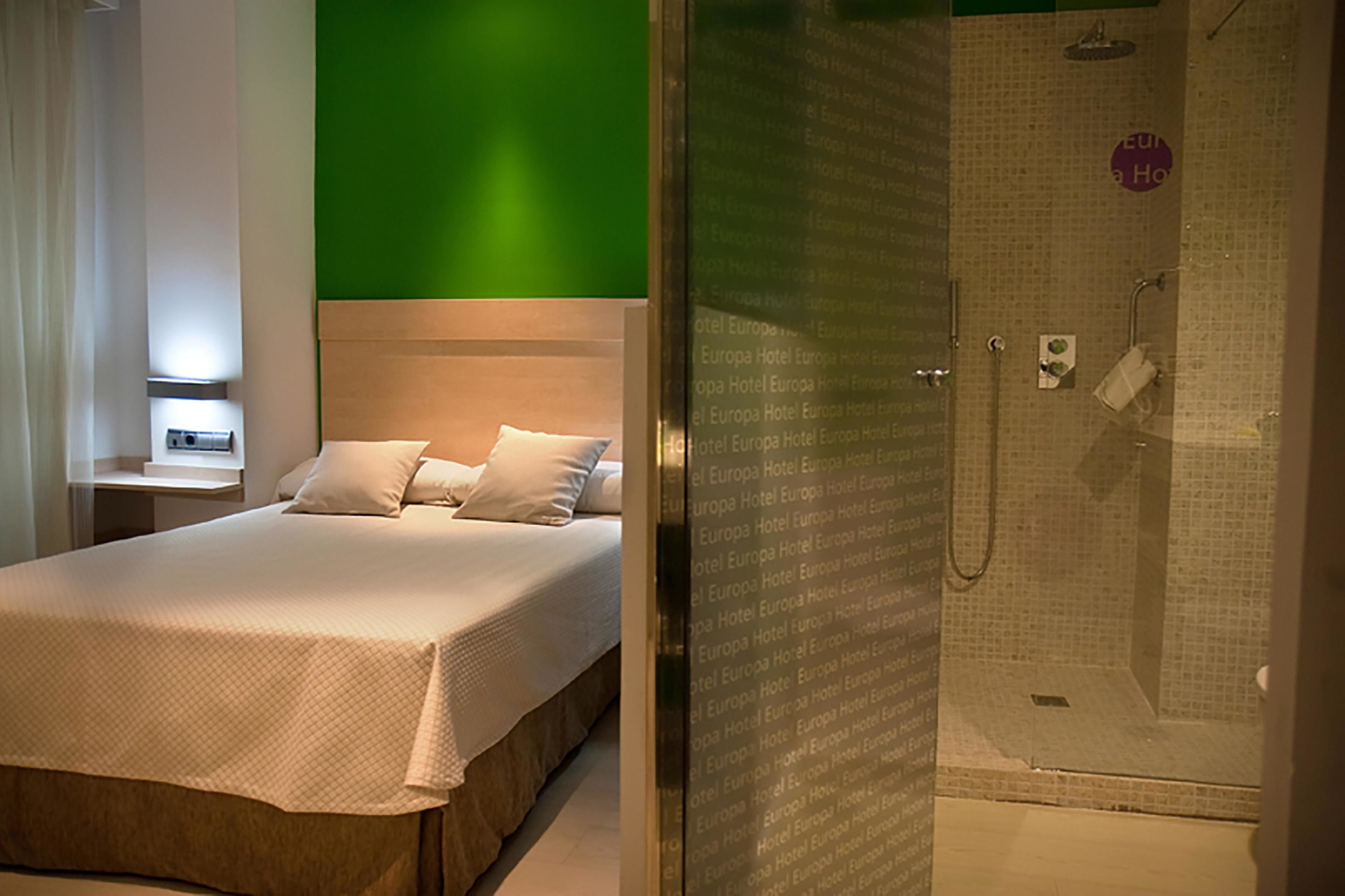 Una habitación de hotel con cama, mesita de noche y zona de ducha.