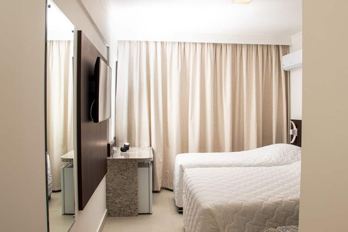 A hotel room with a bed, a desk, a mirror, and a TV.