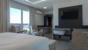 A hotel room with a large bed, a desk with a chair, a TV mounted on the wall, and a window with curtains.