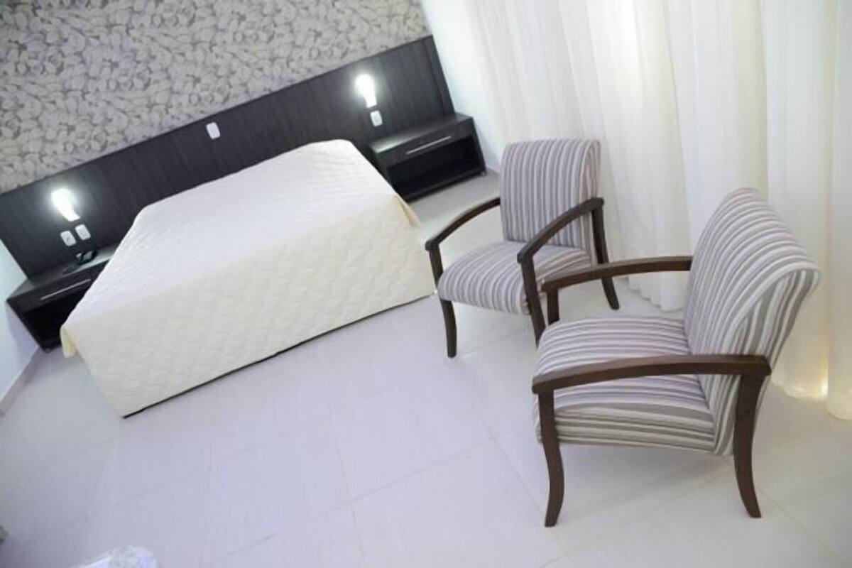 A hotel room with a bed, a chair, a nightstand, and a wall with a patterned design.