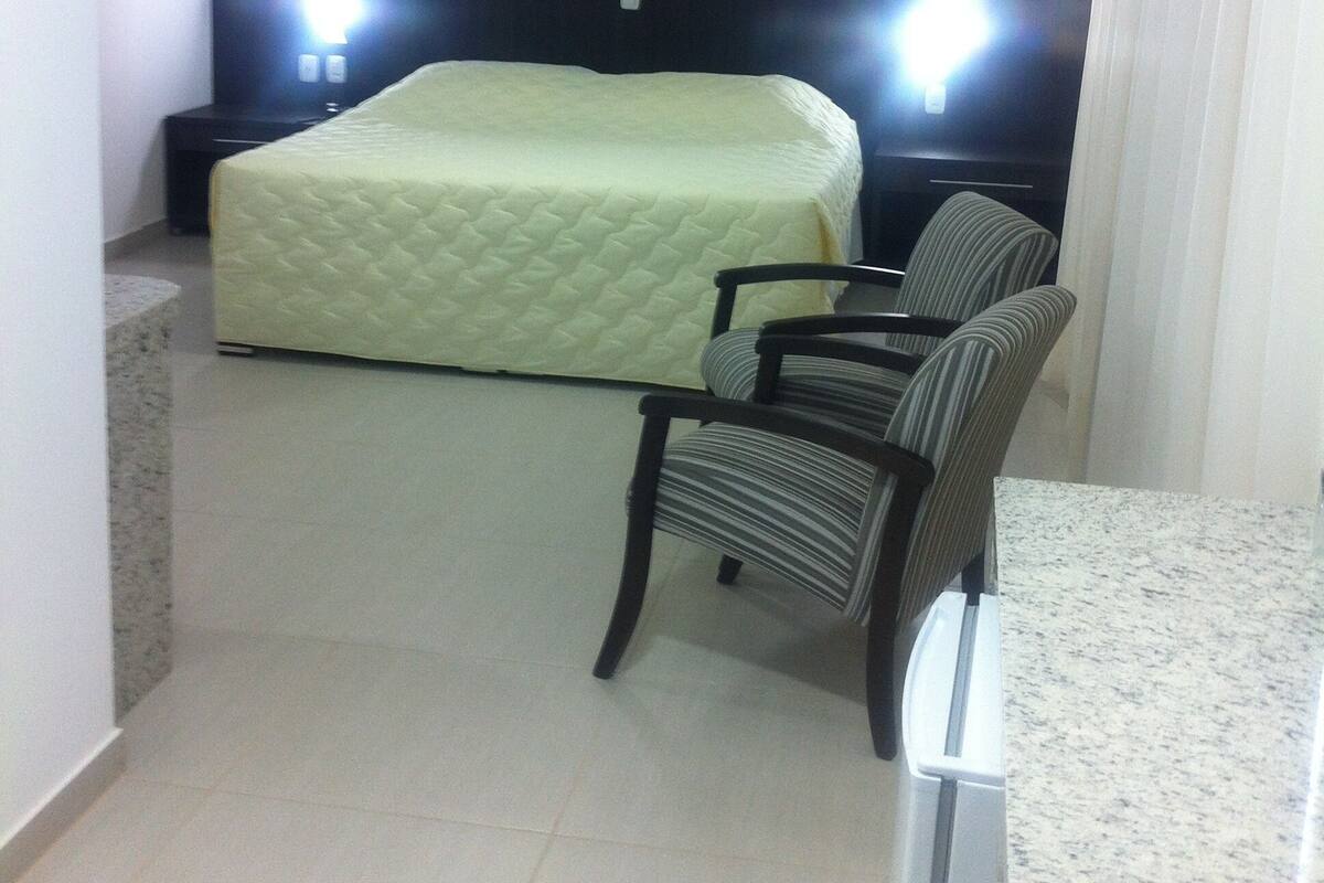 A hotel room with a bed, a chair, a nightstand, a television, and a ceiling light fixture.