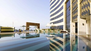 A modern hotel pool area with a clear view of the pool, lounge chairs, and a distinctive building with a unique facade.