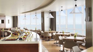 A modern hotel lobby with a curved reception desk, seating area, and large windows offering a city view.