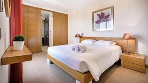 Une chambre d’hôtel moderne avec un lit en bois, deux lampes de chevet, une plante en pot et une grande œuvre d’art florale accrochée au mur.