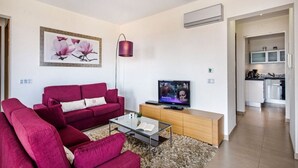 Un salon moderne avec un canapé rouge, une table basse en verre, un téléviseur à écran plat et un tableau représentant des fleurs accroché au mur.