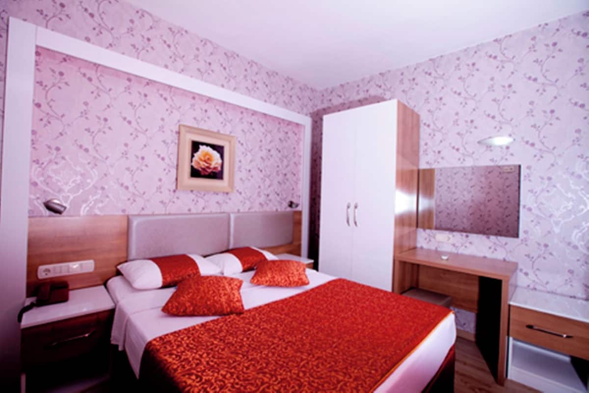 A hotel room with a bed, bedside table, wardrobe, desk, and a mirror.