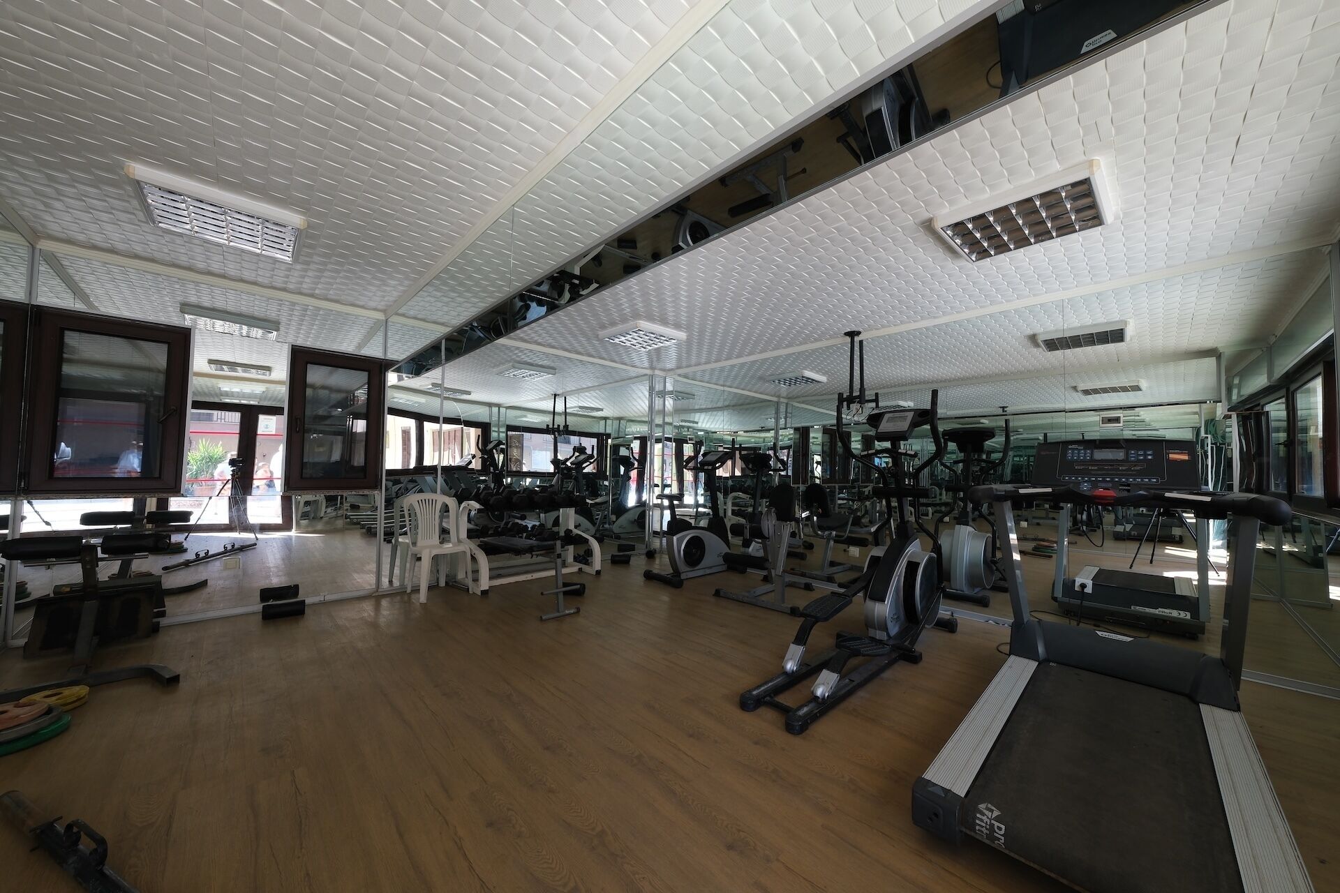 Un gimnasio amplio con diverso equipo de ejercicio, espejos grandes y suelo de madera.
