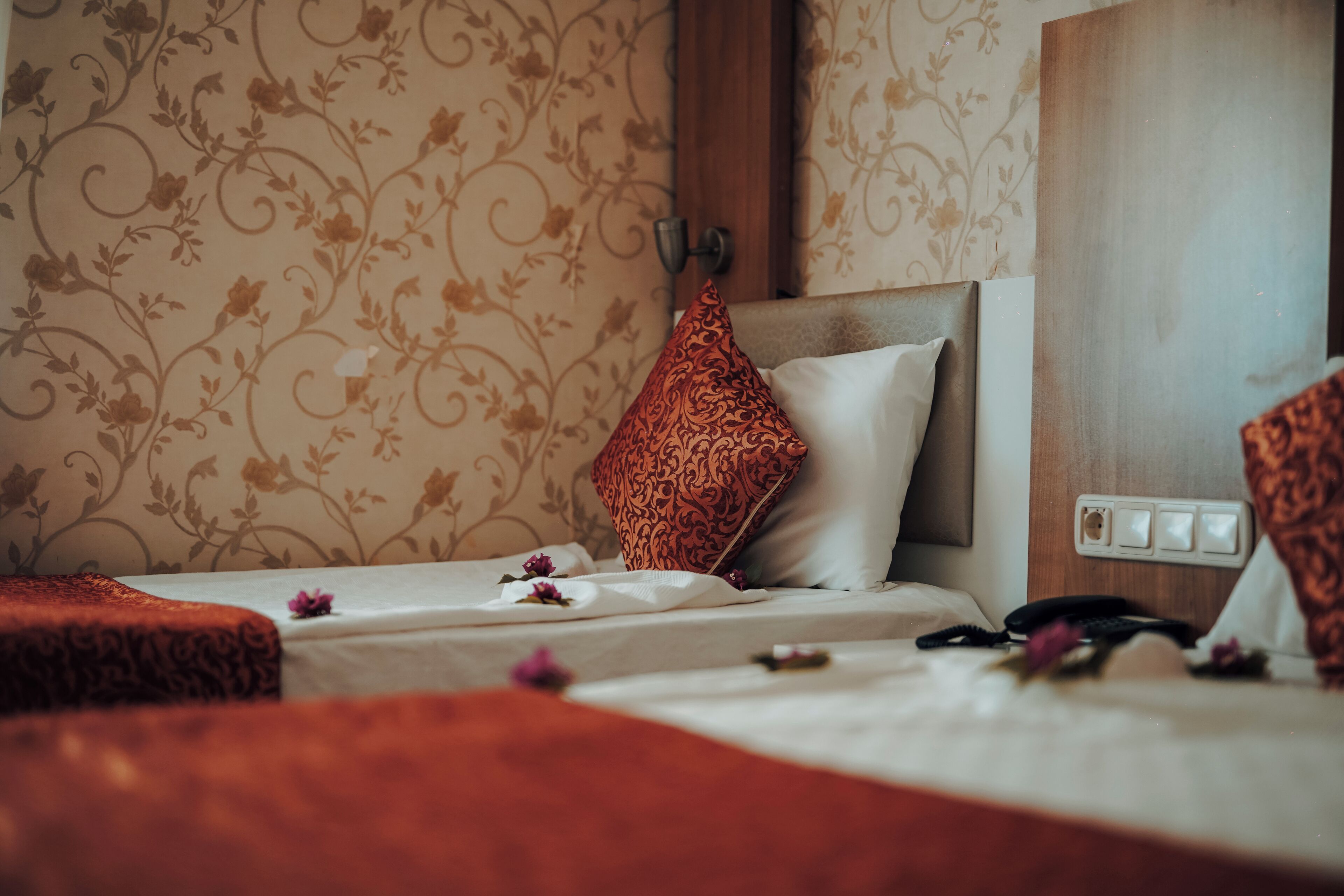 A hotel room with a bed, a telephone, and a wall with floral wallpaper.