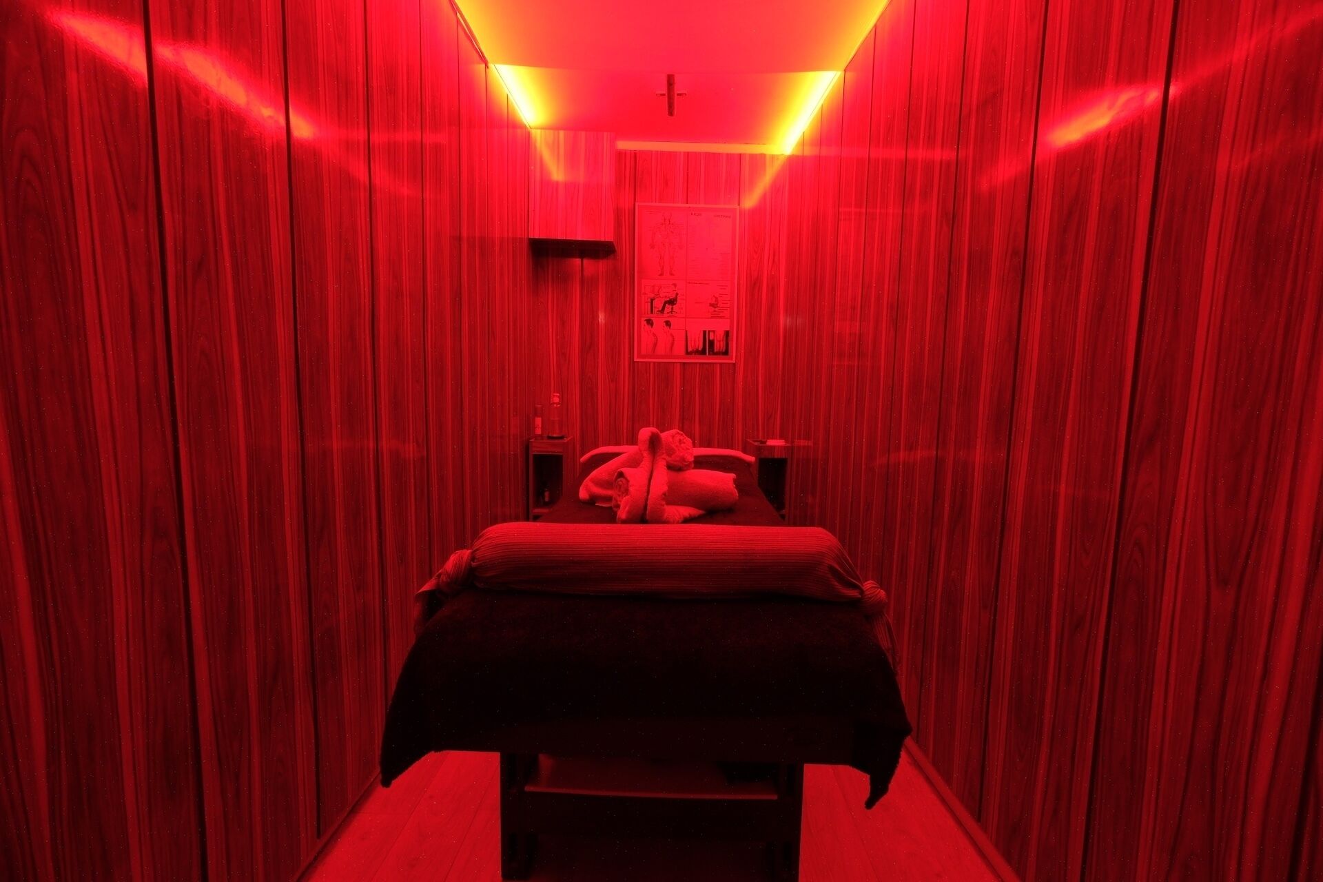 Una habitación estrecha, iluminada con luz roja, con una cama y un cartel en la pared.