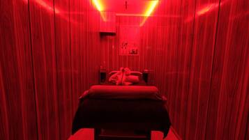 Una habitación estrecha, iluminada con luz roja, con una cama y un cartel en la pared.