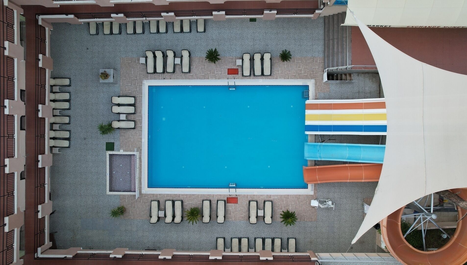 An aerial view of a pool area with a rectangular pool, multiple lounge chairs, and a water slide.