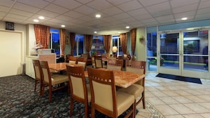 Un comedor de hotel con varias mesas y sillas, un reloj en la pared y vistas a través de puertas de cristal.