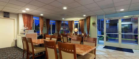 A hotel dining area with multiple tables and chairs, a clock on the wall, and a view through the glass doors.