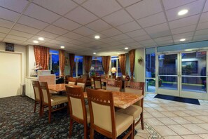 A hotel dining area with multiple tables and chairs, a clock on the wall, and a view through the glass doors. - Ramada by Wyndham Seatac Airport North (Tukwila)
