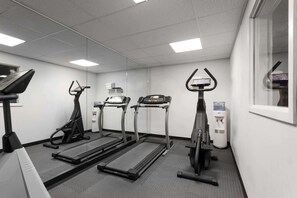 Une salle de sport équipée de tapis de course, de vélos elliptiques et d’un distributeur d’eau.