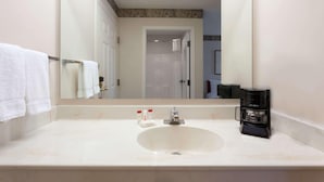 Un baño con un lavamanos blanco, un espejo y una cafetera.