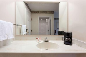 A bathroom with a white sink, a mirror, and a coffee maker. - Ramada by Wyndham Seatac Airport North (Tukwila)