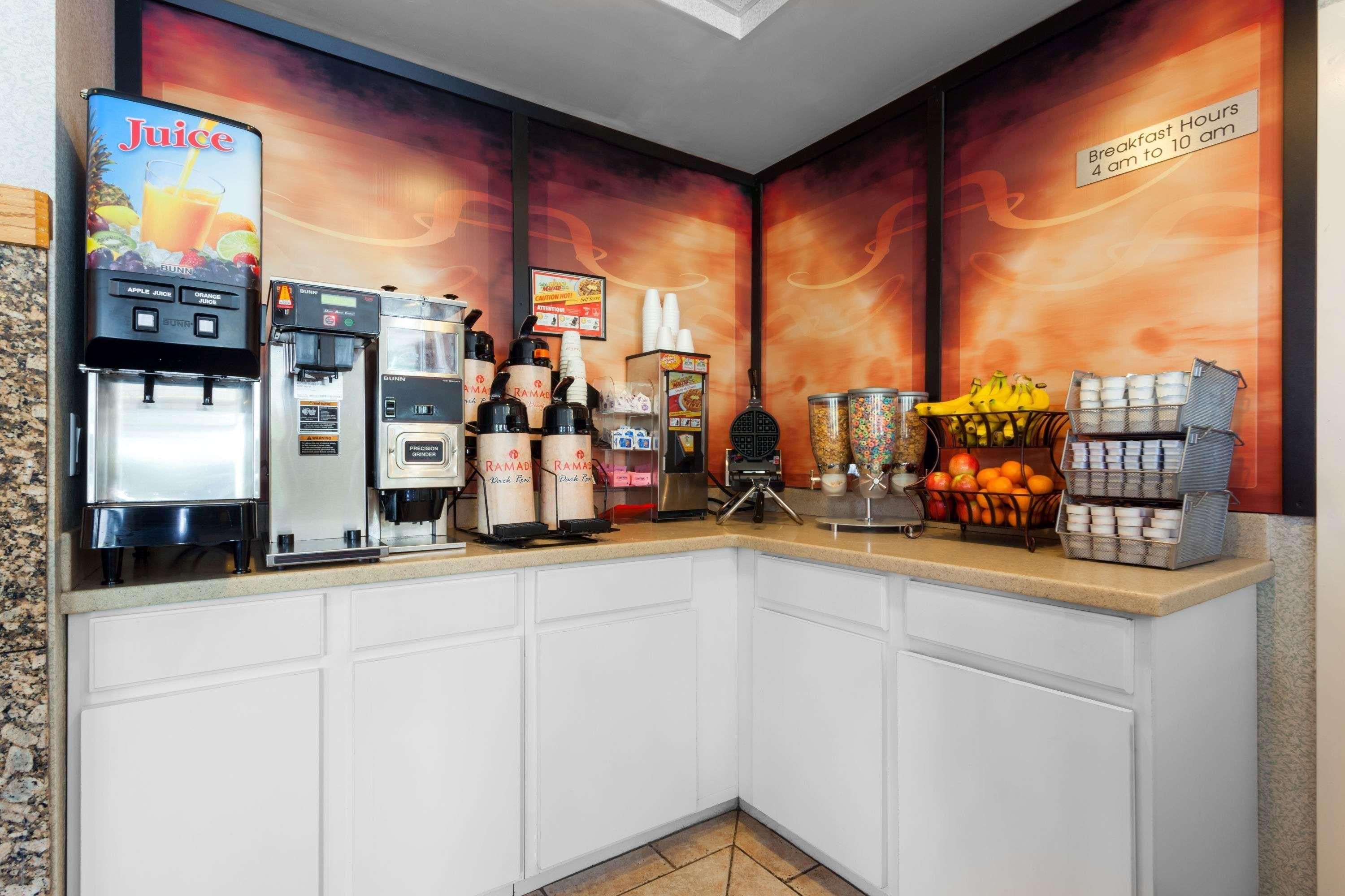 Un comptoir pour le petit-déjeuner avec des distributeurs de jus, des machines à café et un présentoir de fruits.