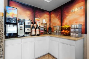 Un comptoir pour le petit-déjeuner avec des distributeurs de jus, des machines à café et un présentoir de fruits.