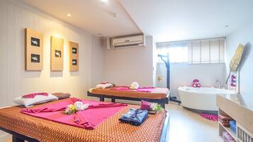 A spa room with two massage beds, a bathtub, and a vanity with a mirror.
