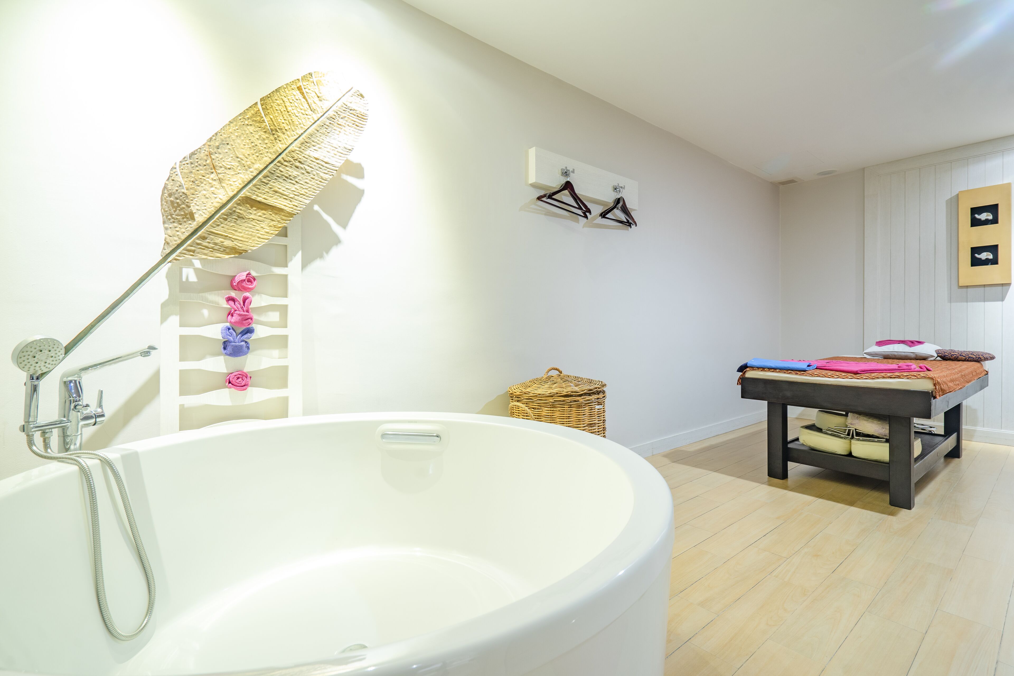 A bathroom with a large bathtub, a showerhead, a wall-mounted towel rack, and a small wicker basket.