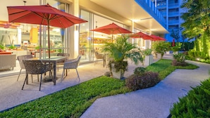Une terrasse extérieure avec des tables et des chaises, des parasols rouges et des plantes en pot.