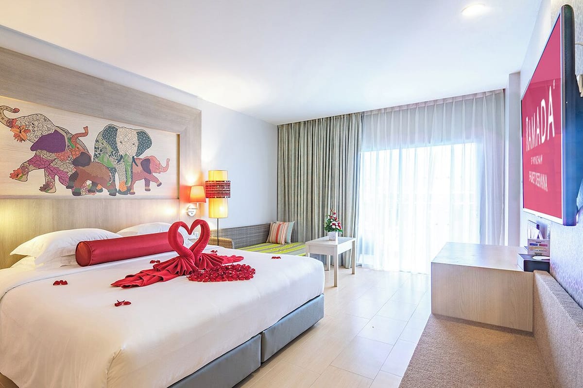 Een hotelkamer met een groot bed, een wandgemonteerde televisie, een bureau en een raam met gordijnen.
