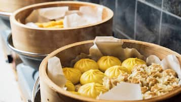 A close-up of a bamboo steamer basket filled with yellow steamed buns and a wooden tray with white dumplings.