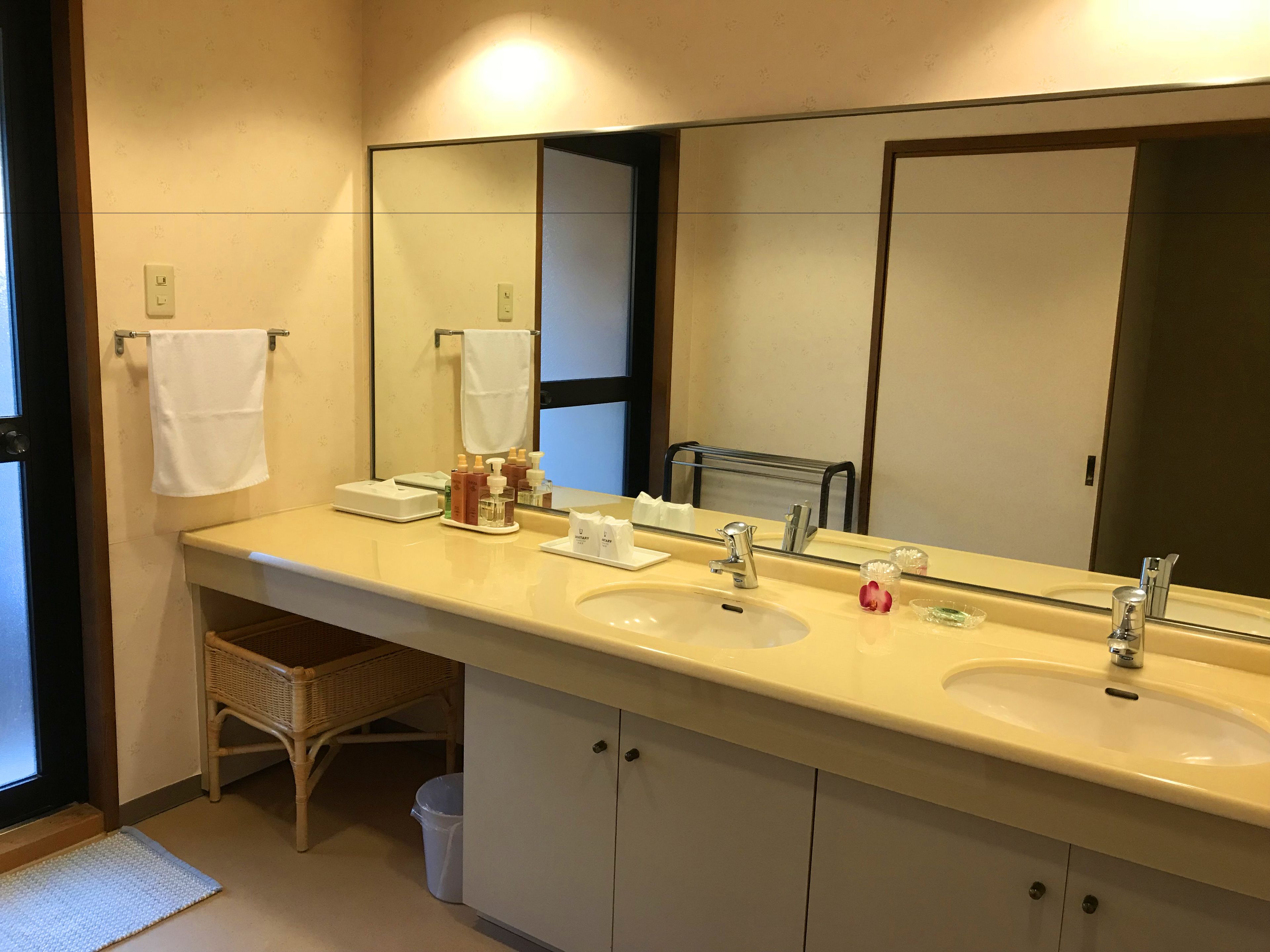 Un baño con dos lavamanos, un espejo grande y una silla de mimbre.