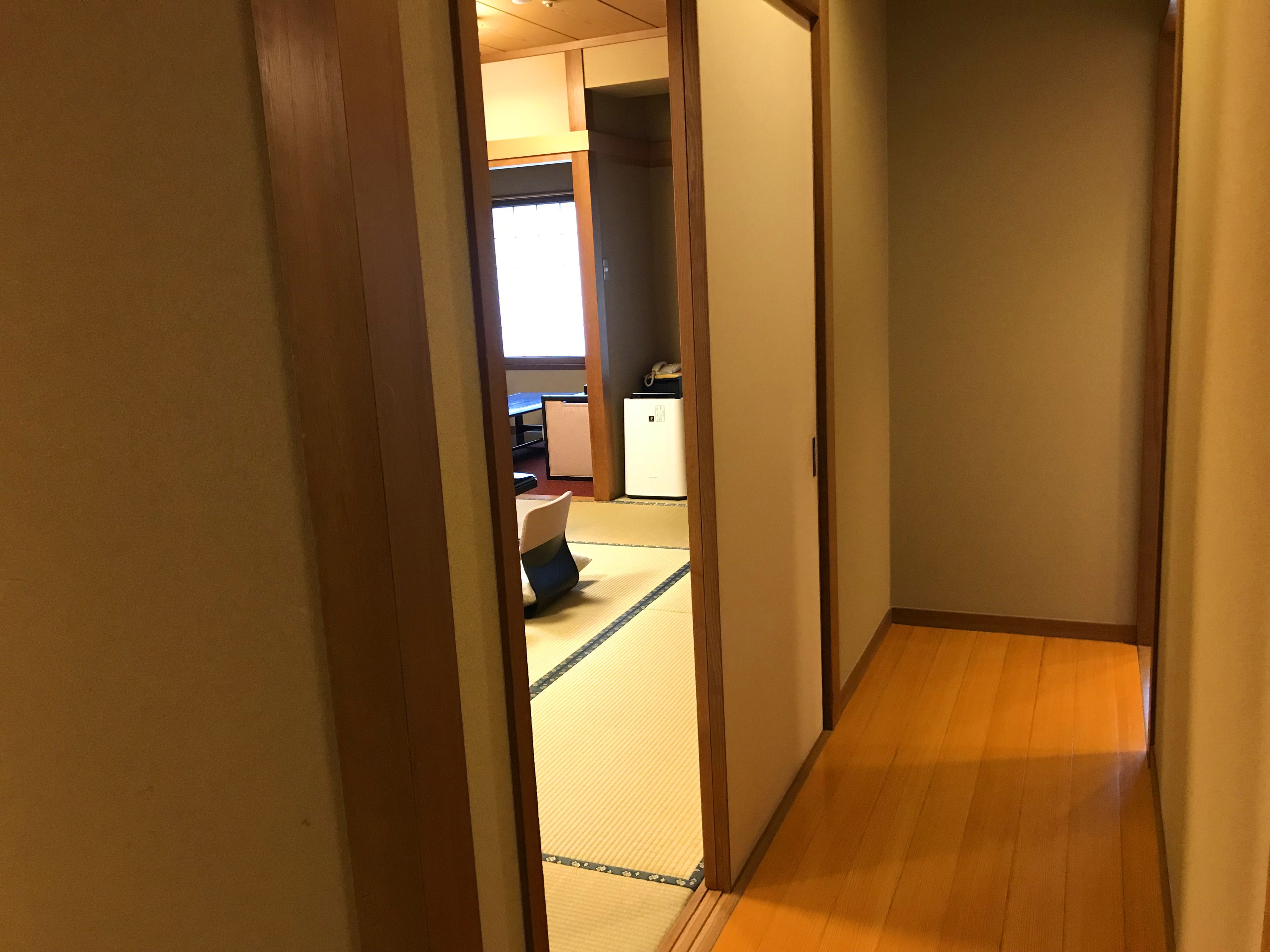 A narrow hallway with wooden flooring and a tatami mat area at the end.