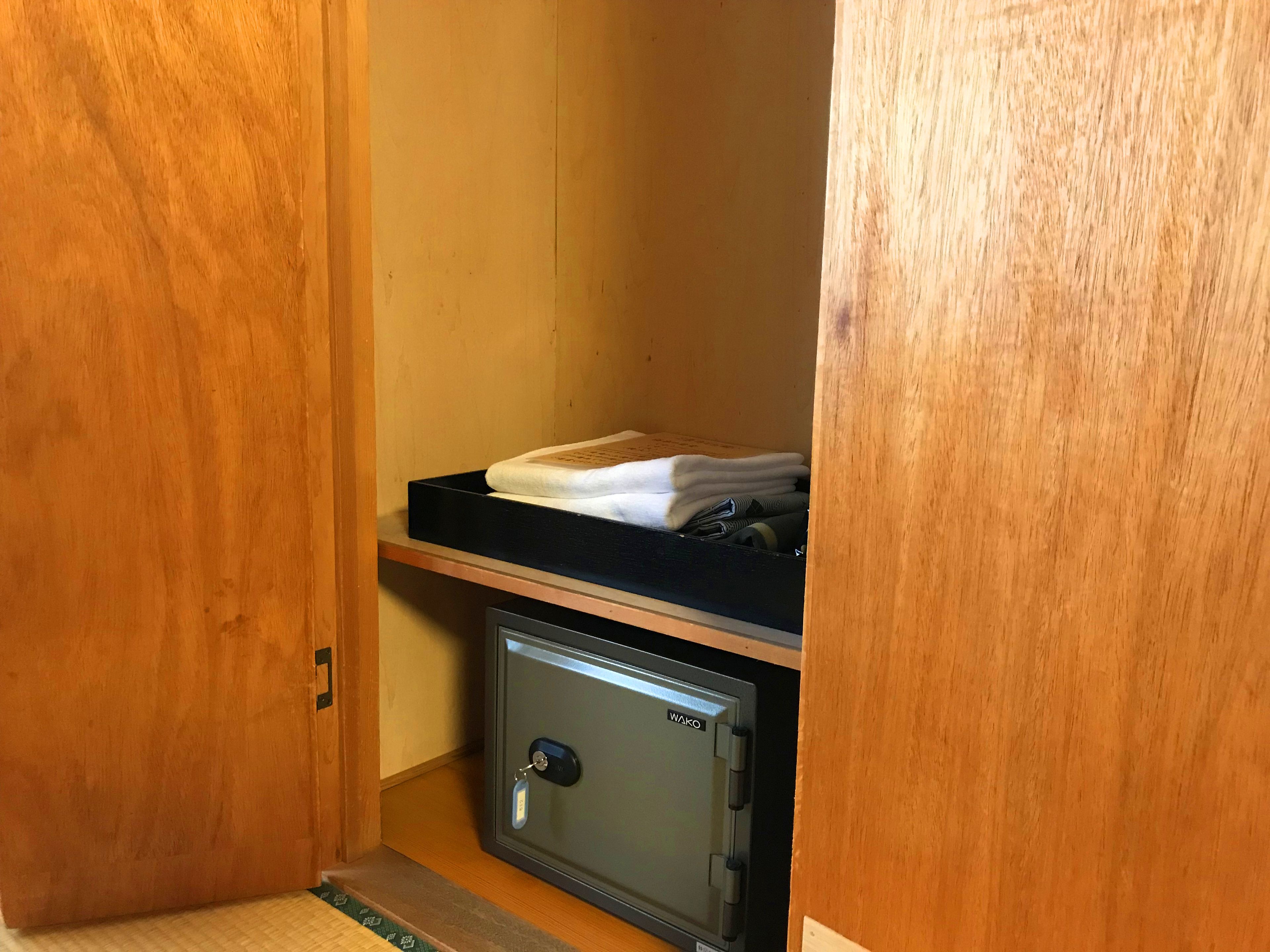 A small storage space with a black shelf holding folded towels and a Wako safe.
