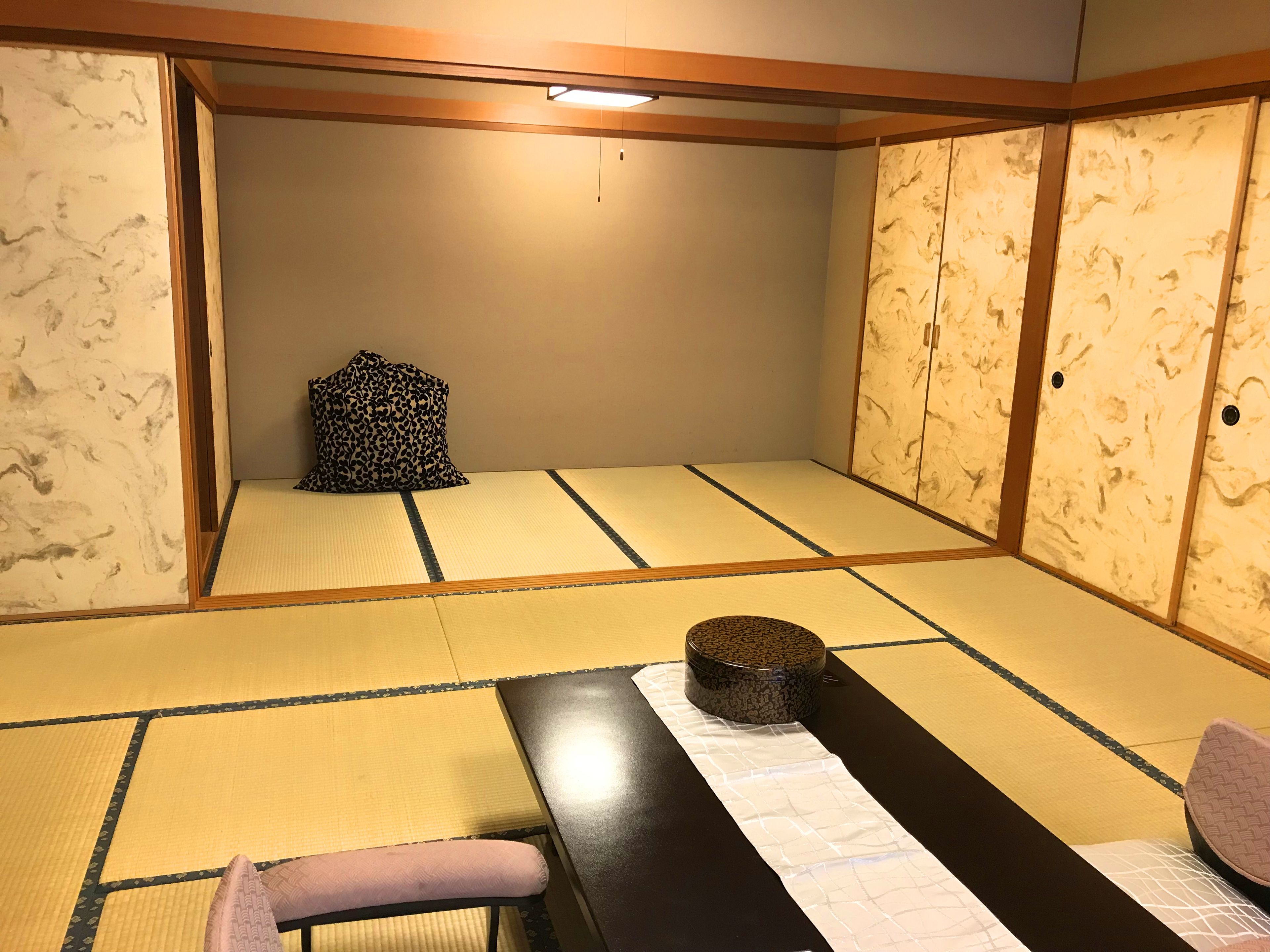 A tatami mat room with a low table, a cushion, and a traditional Japanese pillow.