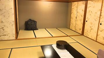 A tatami mat room with a low table, a cushion, and a traditional Japanese pillow.