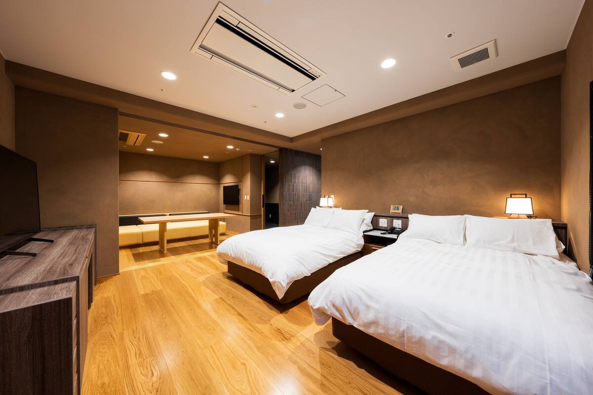 A hotel room with two beds, a desk, and a seating area.