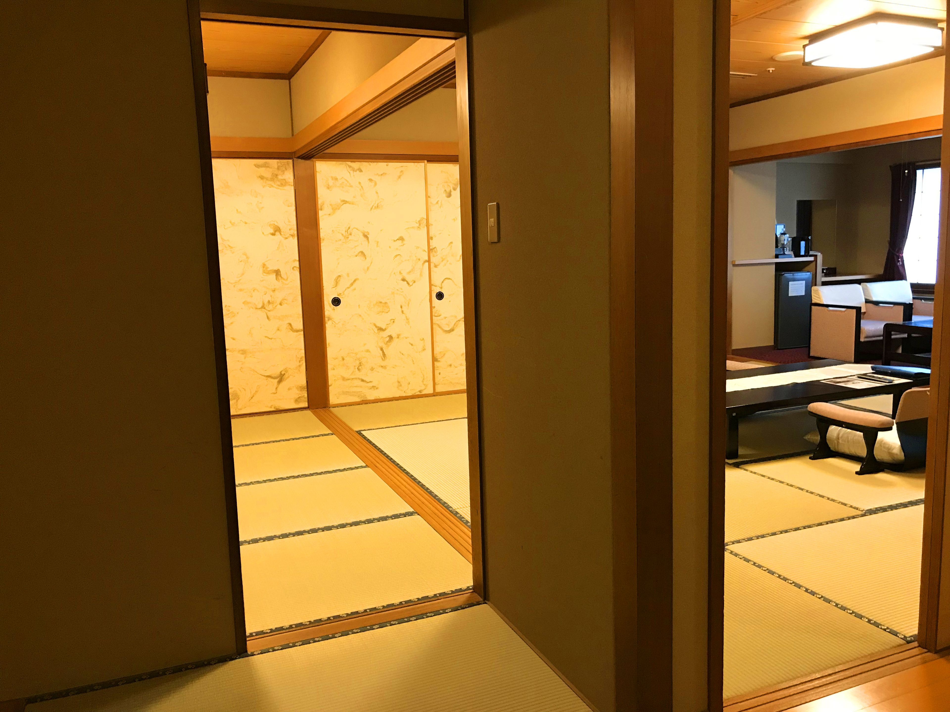 A traditional Japanese room with tatami flooring, a low table with cushions, and a sliding door leading to another room.